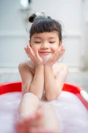 bath child girl|Young girl sitting in a large sink, having a foam bath, playing with water  running from a faucet. stock photo